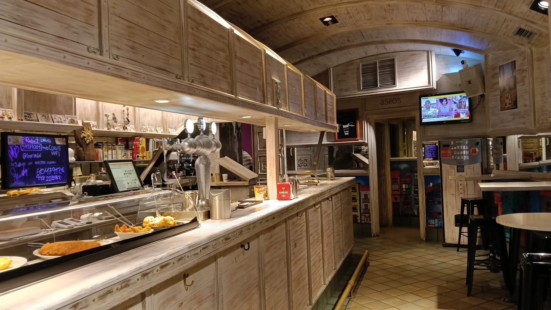 La barra de El Redín Gastrobar, en madera clara, con los tiradores de cerveza y la vitrina de pintxos; al fondo, el techo abovedado de madera.