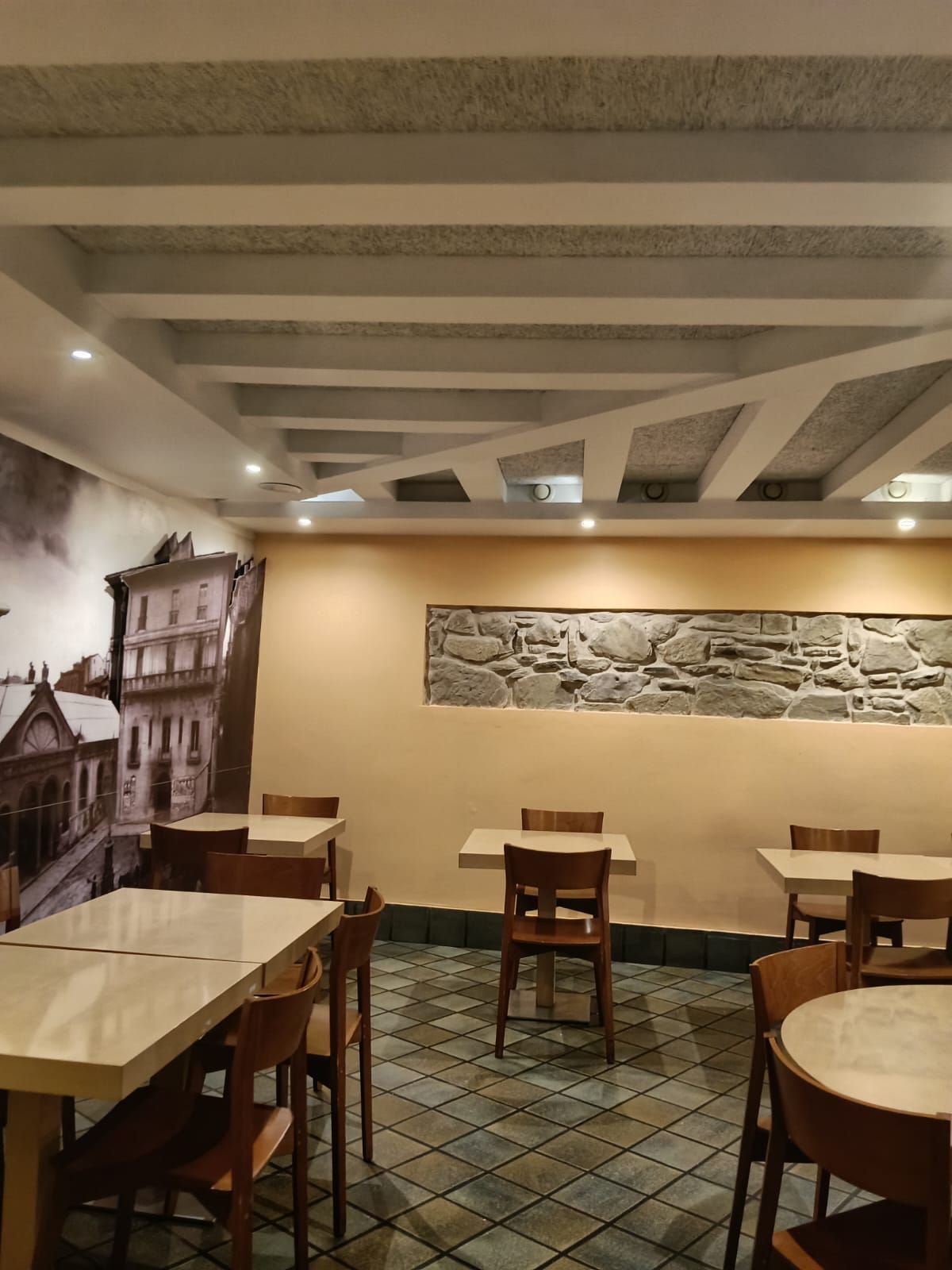El fondo del comedor, con el tramo de muro de piedra iluminado sobre la pared clara y el techo de vigas.
