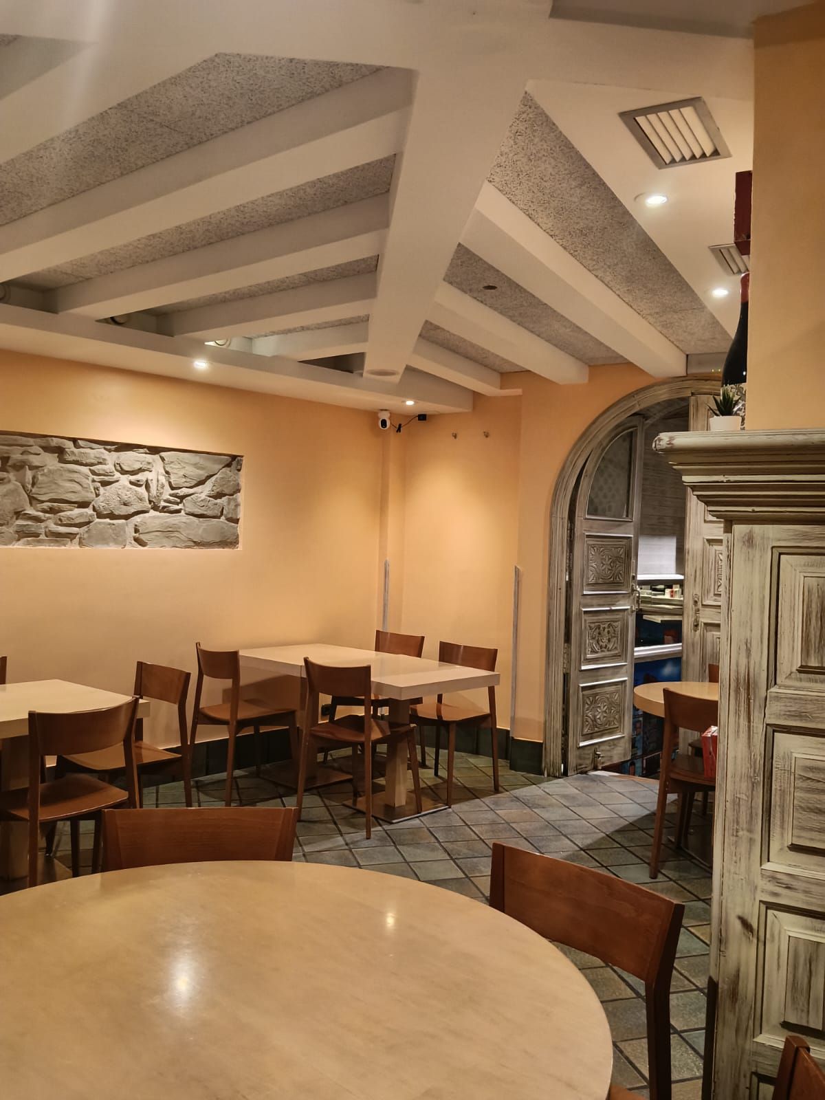 El comedor junto al arco que da a la entrada, con una mesa redonda y el tramo de muro de piedra en la pared.