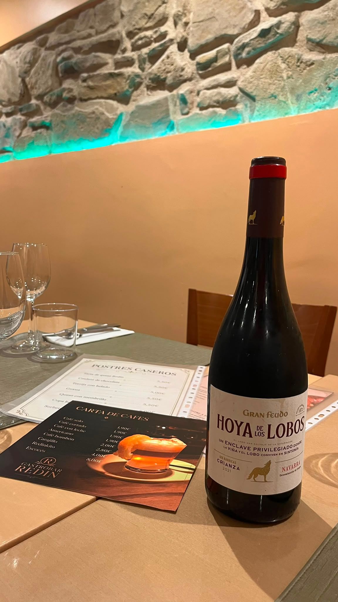 Una botella de vino tinto de Navarra sobre una mesa puesta, con la carta de postres al lado.