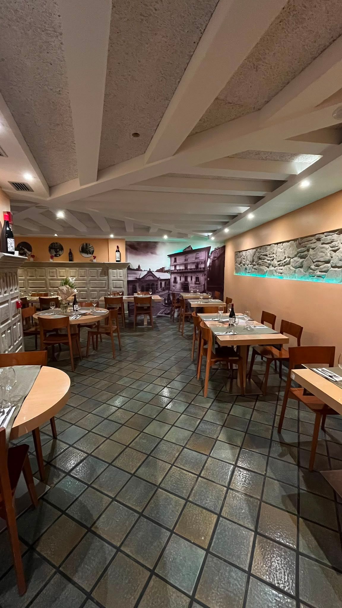 El pasillo del comedor con las mesas puestas a los dos lados y el muro de piedra iluminado.