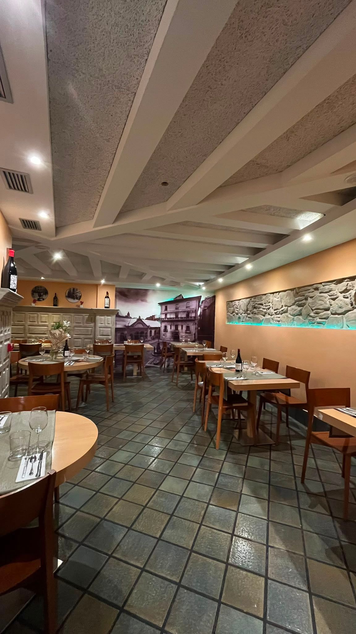 El comedor a lo largo, con las mesas puestas y el techo de vigas blancas.