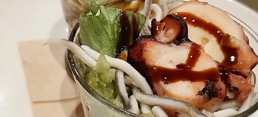 Dos vasitos de cristal con rodajas de pulpo sobre gulas y lechuga, regados con una reducción oscura.