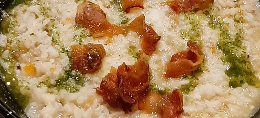 Una cazuela negra con arroz cremoso, trozos de carne dorada por encima y aceite verde de hierbas.
