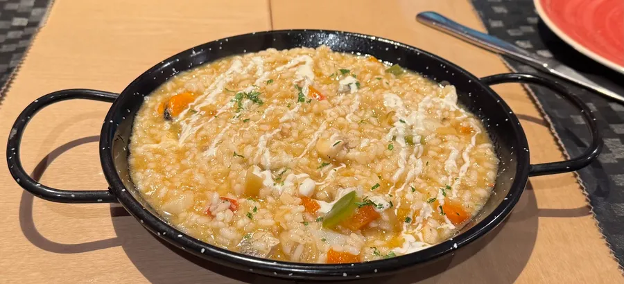 Una cazuela negra con arroz caldoso con verduras en dados y un hilo de salsa blanca por encima.