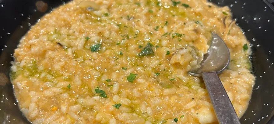 Una cazuela negra con arroz caldoso con perejil y aceite verde, con la cuchara dentro.