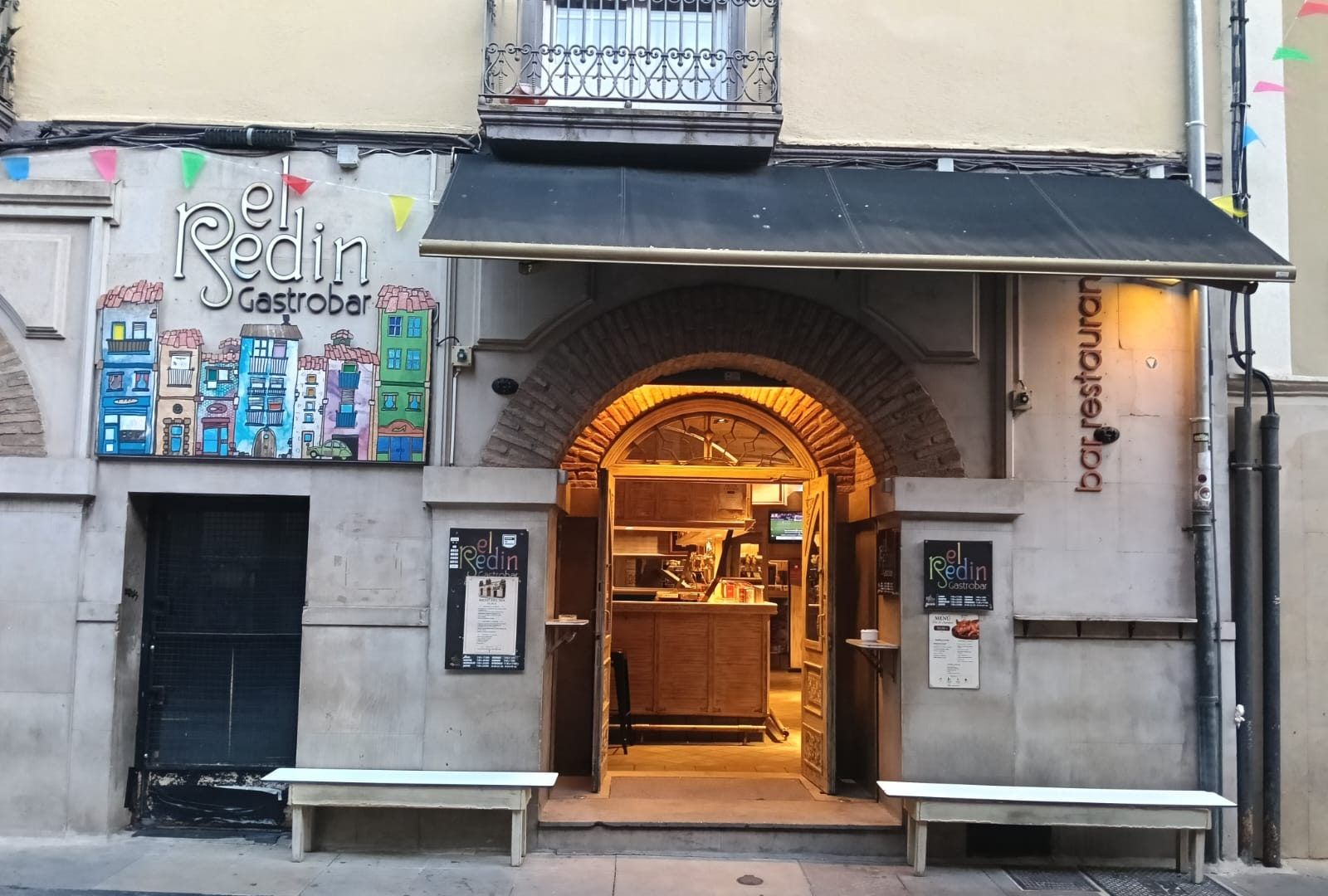 La fachada de El Redín Gastrobar en la calle Mercado, con la puerta de arco abierta, las cartas colgadas a los lados y el rótulo pintado a mano con casas de colores.