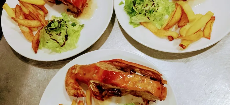 Tres platos de gorrín al horno recién emplatados, con patatas fritas gruesas y ensalada.