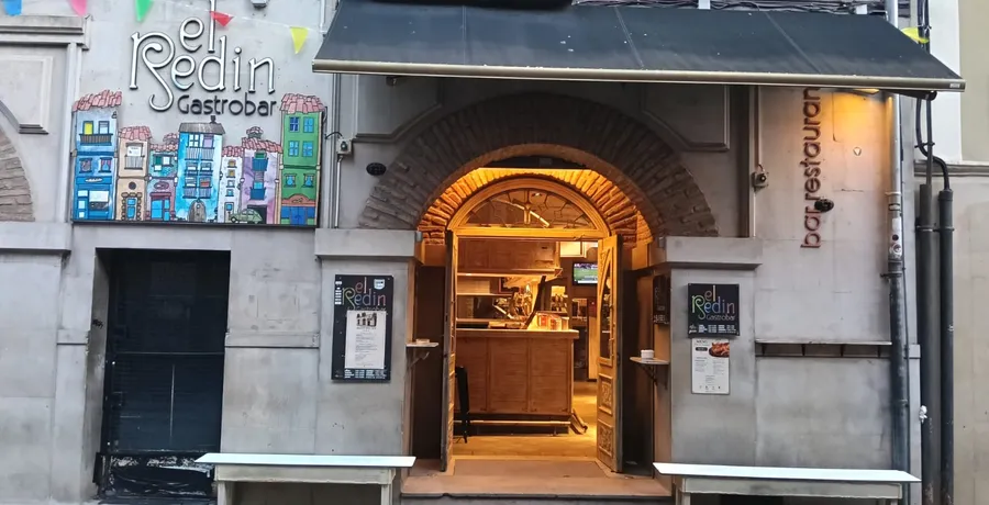 La fachada de El Redín Gastrobar en la calle Mercado, con la puerta de arco abierta, las cartas colgadas a los lados y el rótulo pintado a mano con casas de colores.