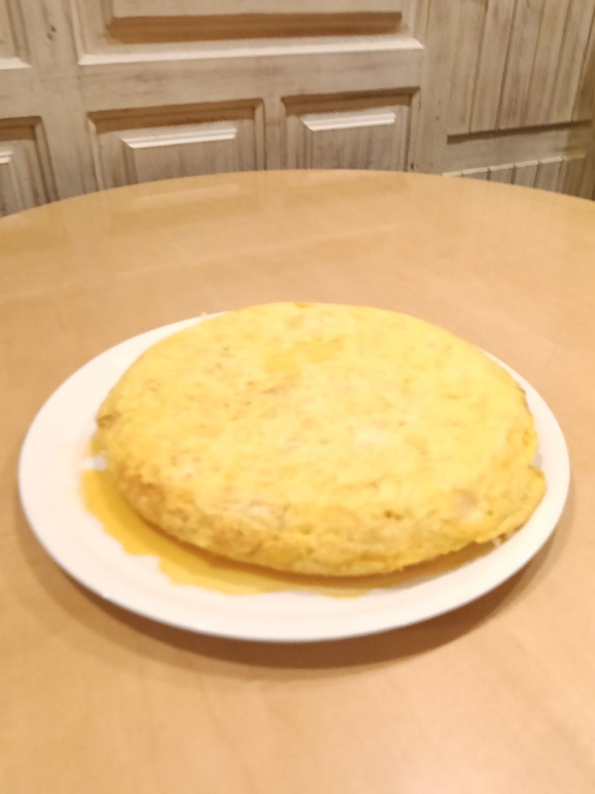 Una tortilla de patata entera y jugosa en un plato blanco, sobre una de las mesas del comedor.